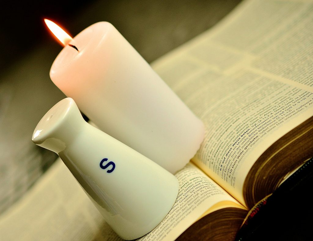 Salz und Licht sollen wir sein, nicht Zucker oder Senf: Ein Salzstreuer und eine brennende Kerze auf einer Bibel