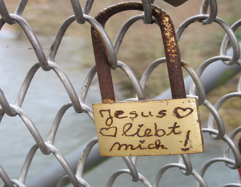 Ein Vorhängeschloss an einem Zaun mit der Aufschrift: "Jesus liebt mich"