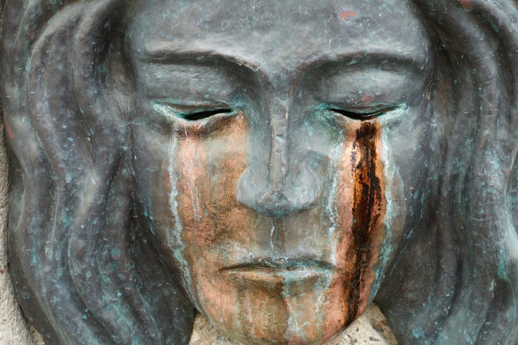 Skulptur eines Gesichts, auf dem Tränenspuren zu sehen sind