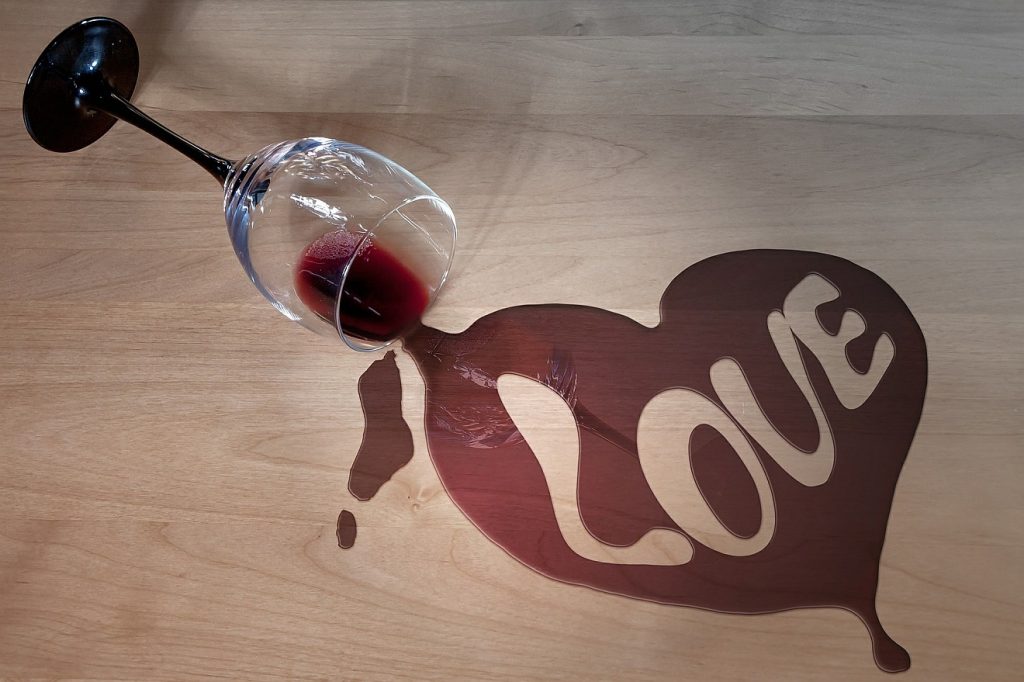 Alkoholabhängigkeit zerstört Ehe und Familie: Im Wein, der aus einem umgefallenen Weinglas auf einen Tisch läuft, steht das Wort "Love" = "Liebe"