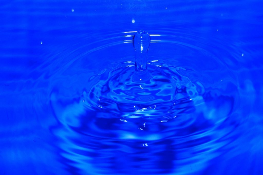 Ein Wassertropfen fällt in blaues Wasser und springt hoch