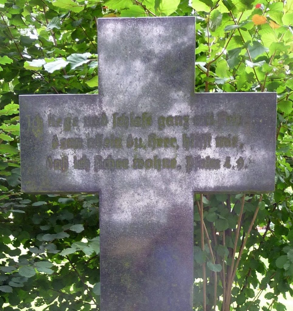 Grabkreuz aus Stein mit Inschrift: "Ich liege und schlafe ganz mit Frieden..."