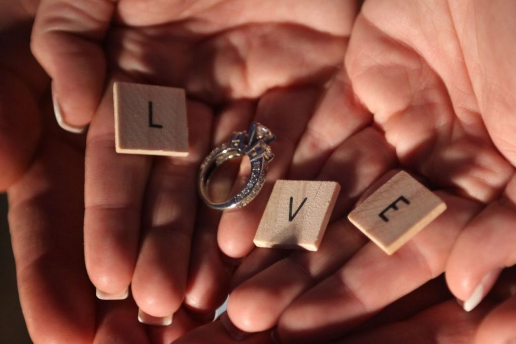 Das Wort LOVE = Liebe wird von drei Scrabble-Buchstaben und einem Ehering gebildet, die in zwei Händen liegen.
