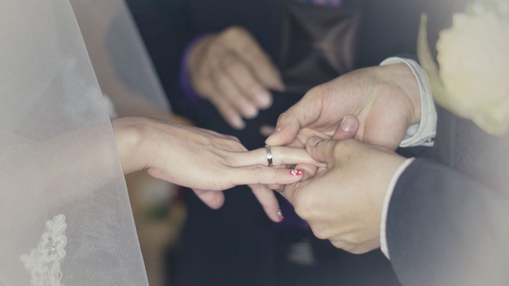 Beim Ringsegen während der kirchlichen Trauung sind die Hände des Ehemannes zu sehen, der seiner Frau den Ring auf den Finger steckt.