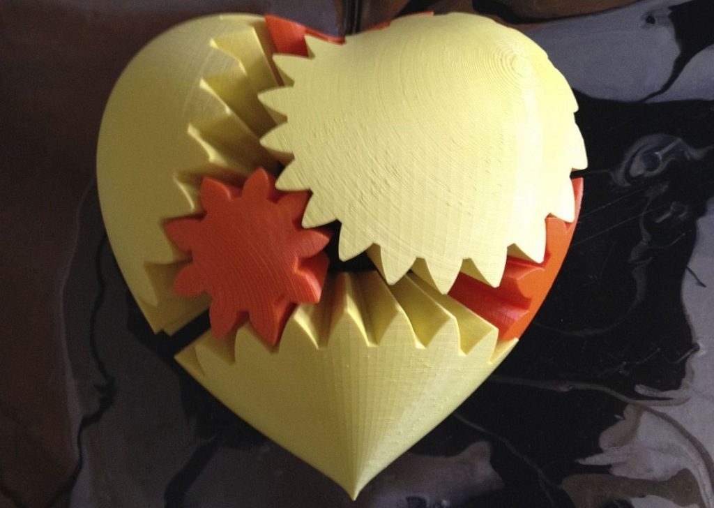 Ein massiv erscheinendes Herz besteht aus mehreren ineinander greifenden Zahnrädern in gelber und roter Farbe.