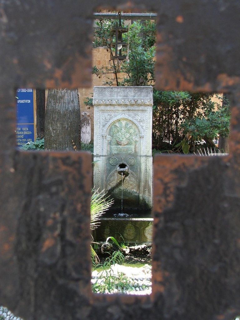 Durchblick durch ein Kreuz auf einen Brunnen