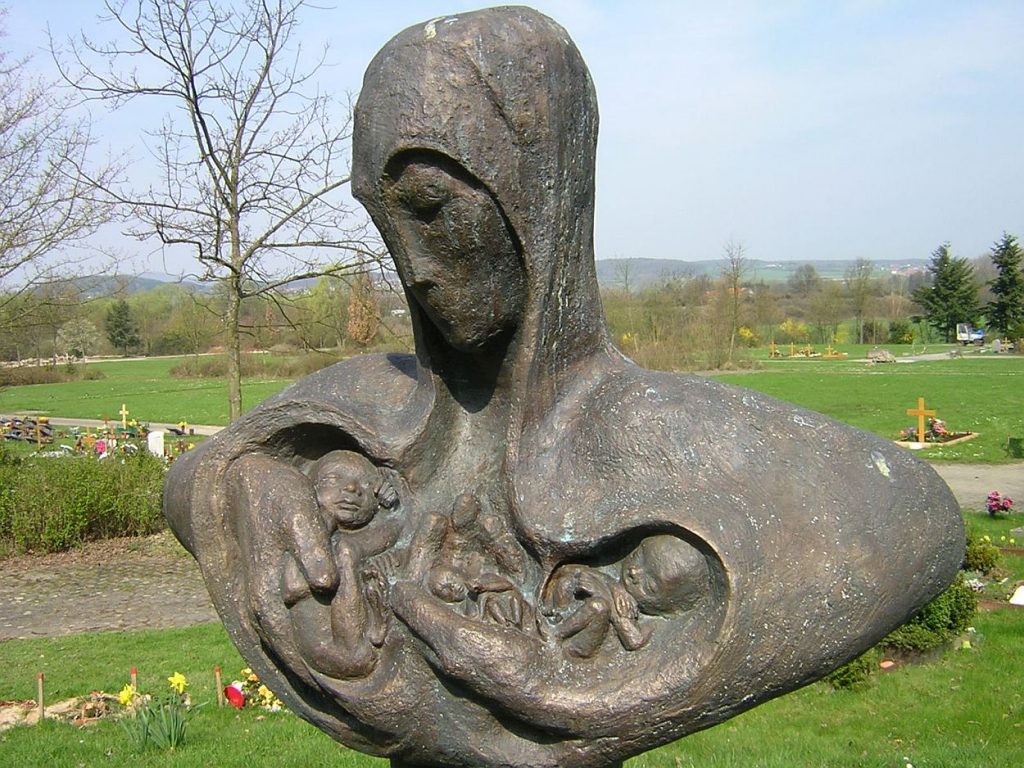 Geboren, um sogleich zu sterben: Die Bronze-Skulptur „Geborgen“ stellt eine Frau dar, die in ihren Armen bzw. in ihrer Brust mehrere totgeborene Kinder umfasst