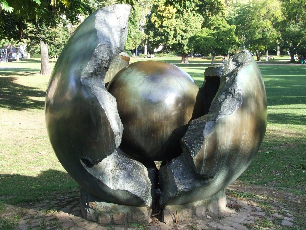 Bronze-Kunstwerk im Park: Eine kleine Kugel erscheint in der aufgebrochenen Schale einer großen Kugel