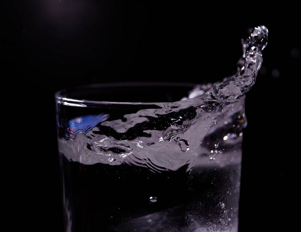 Ein Glas Wasser vor schwarzem Hintergrund, in dem das Wasser ein wenig hochspritzt - lebendiges Wasser! 