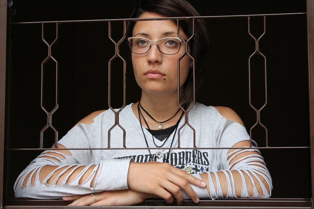 Zwischen Zweifel und Glaube: das Bild einer nachdenklich blickenden jungen Frau hinter einem filigranen Gitter