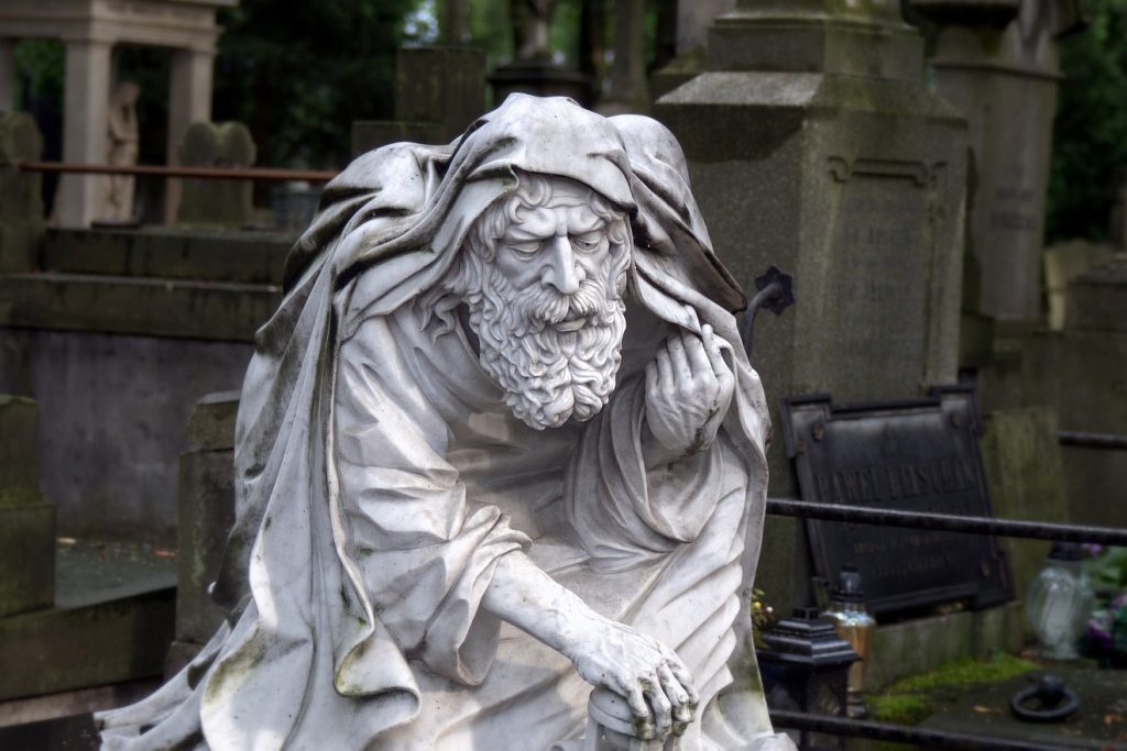 Alt und lebenssatt sterben: Die Skulptur eines gebeugten, sehr alten Mannes auf einem Friedhof