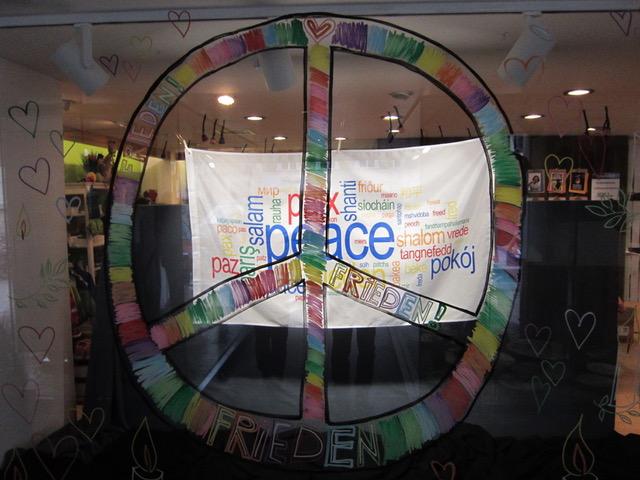 Das Peace-Rad auf einer Scheibe und dahinter ein Tuch mit dem Wort "Frieden" in verschiedenen Sprachen