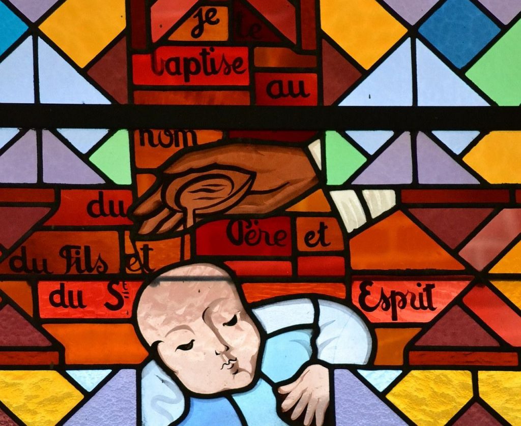 Ein Kirchenfenster mit einem Kind, das getauft wird, mit der französischen Umschriftung: Je baptise au nom du Père et du Fils et du St. Esprit.