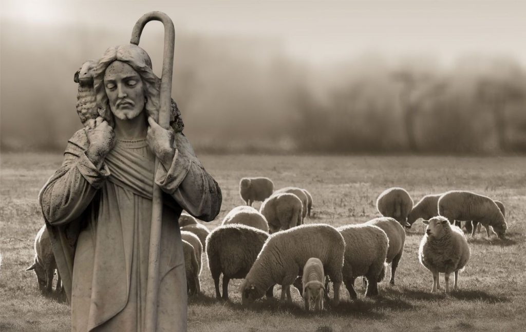 Statue von Jesus mit Hirtenstab und Schaf über den Schultern und im Hintergrund eine Schafherde