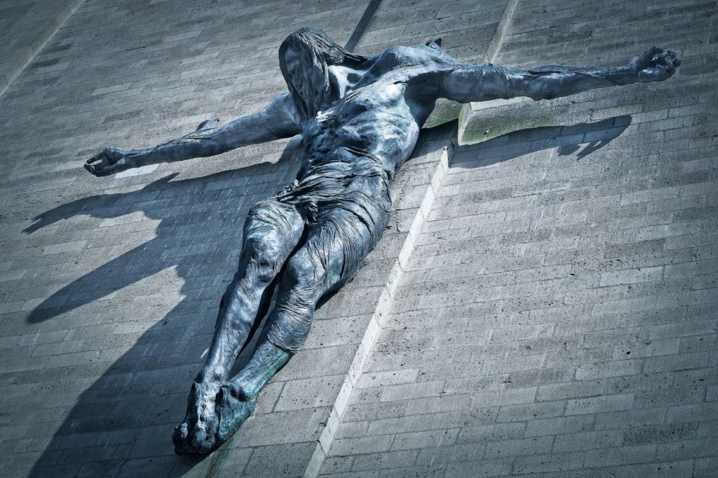 Ein geschundener, zerfleischter Jesus an einer schlichten gemauerten Wand wie am Kreuz ausgestreckt