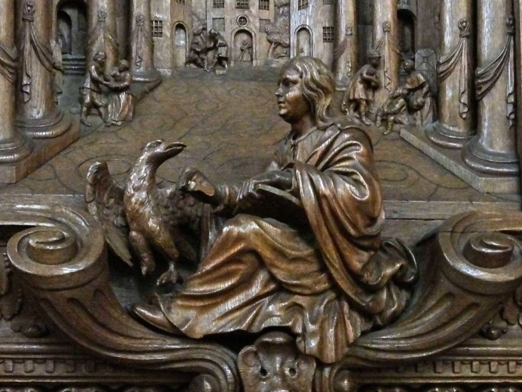 Der Evangelist Johannes ist zusammen mit seinem Symbolbild des Adlers als Holzschnitzerei in einer Kirche zu sehen; im Hintergrund eine Säulenhalle mit verschiedenen Menschen, die in Auseinandersetzungen begriffen zu sein scheinen